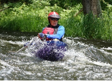 Neil Grossman paddling a purple canoe with a red helmet and lifevest and light blue top in class 1 whitewater